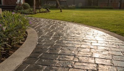 A beautifully designed stamped concrete walkway with a textured stone-like pattern, curving through a landscaped garden for an elegant outdoor upgrade.