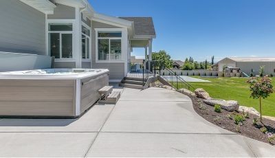 A modern backyard patio with a smooth concrete finish, featuring a built-in hot tub and scenic landscaping, creating a stylish and functional outdoor living space.