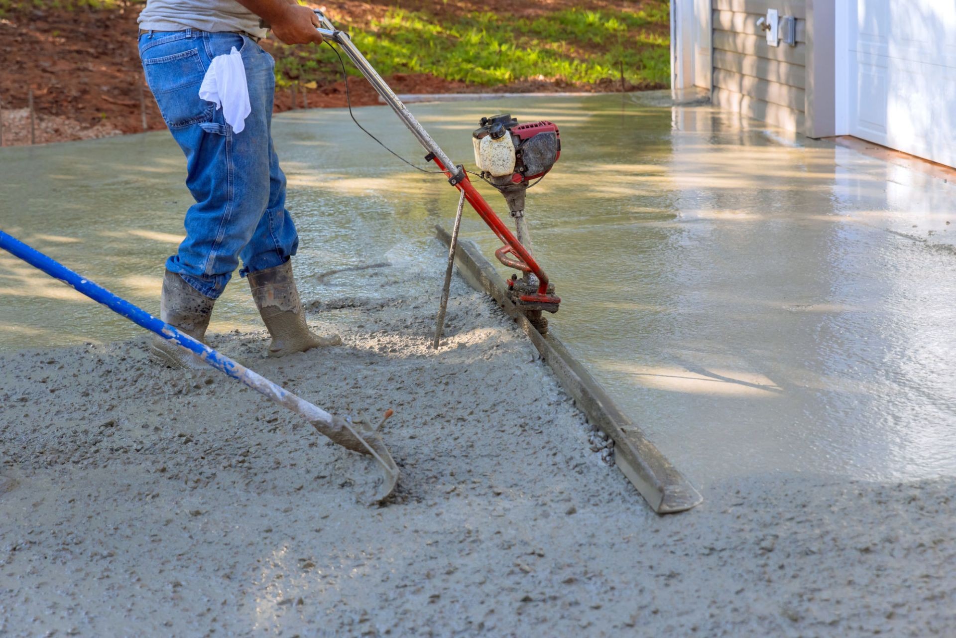 Worker using a tamping machine to smooth and compact concrete for a durable driveway surface.